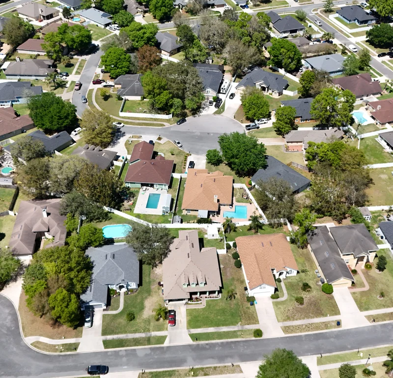 Aerial view of a Tampa neighborhood with Florida-style homes, screened-in pools, and asphalt shingle roofs, illustrating spring roof damage risks from heat, humidity, and rain.